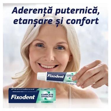 Femeie zambitoare tinand un tub de Fixodent Plus Food Barrier, cu ambalajul cutiei de Fixodent dedesubt. Femeie zambitoare tinand un tub de Fixodent Plus Food Barrier, cu ambalajul cutiei de Fixodent dedesubt.
