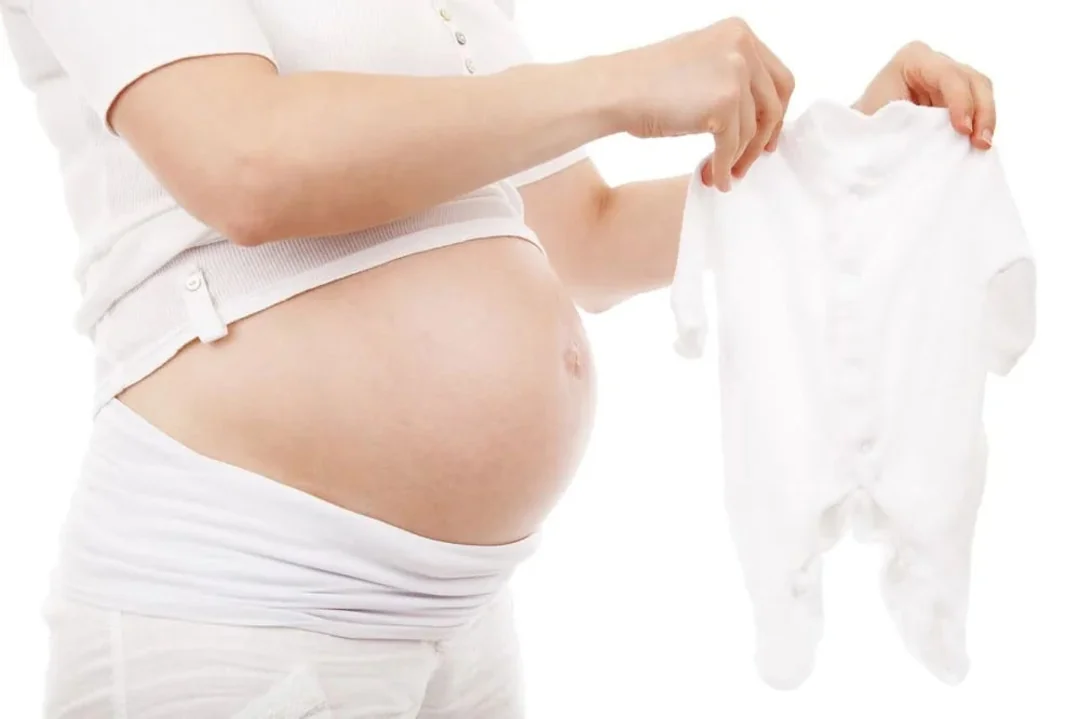 femeie insarcinata cu imbracaminte pentru bebe in maini