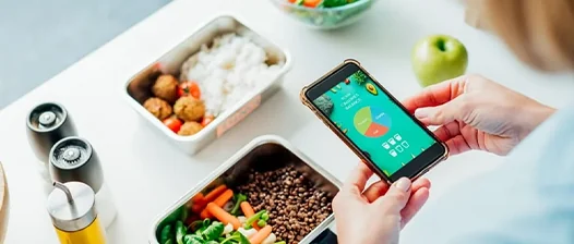 masa pe care se aflta diferite mancaruri sanatoase si persoana care are o aplicatie de monitorizare pe telefon
